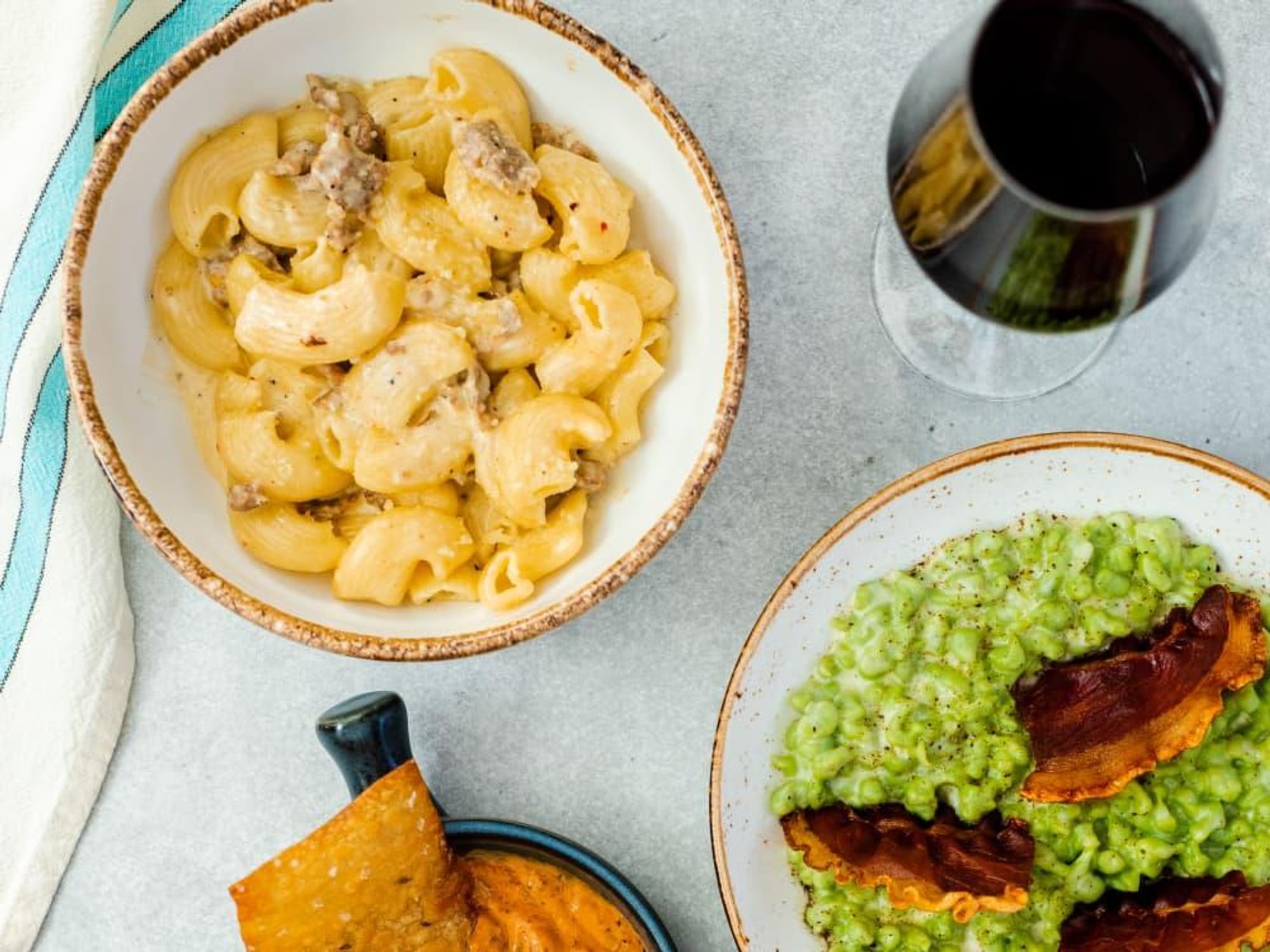 A bowl of macaroni and cheese, wine, hummus, and green risotto.
