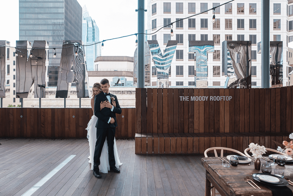 A couple in wedding clothes stands on the Moody rooftop at the Jones Center.