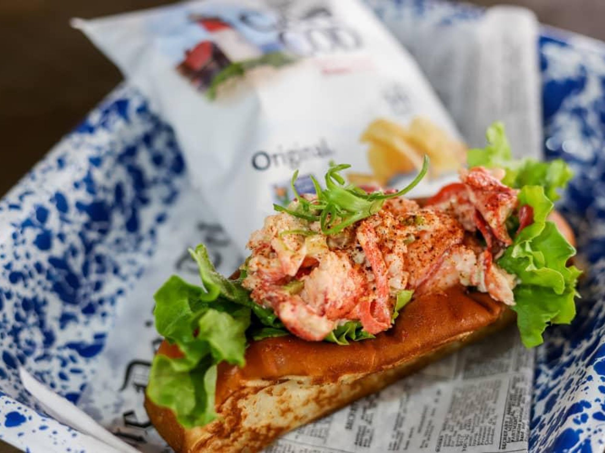 A lobster roll on a blue and white ceramic plate with Cape Cod chips.