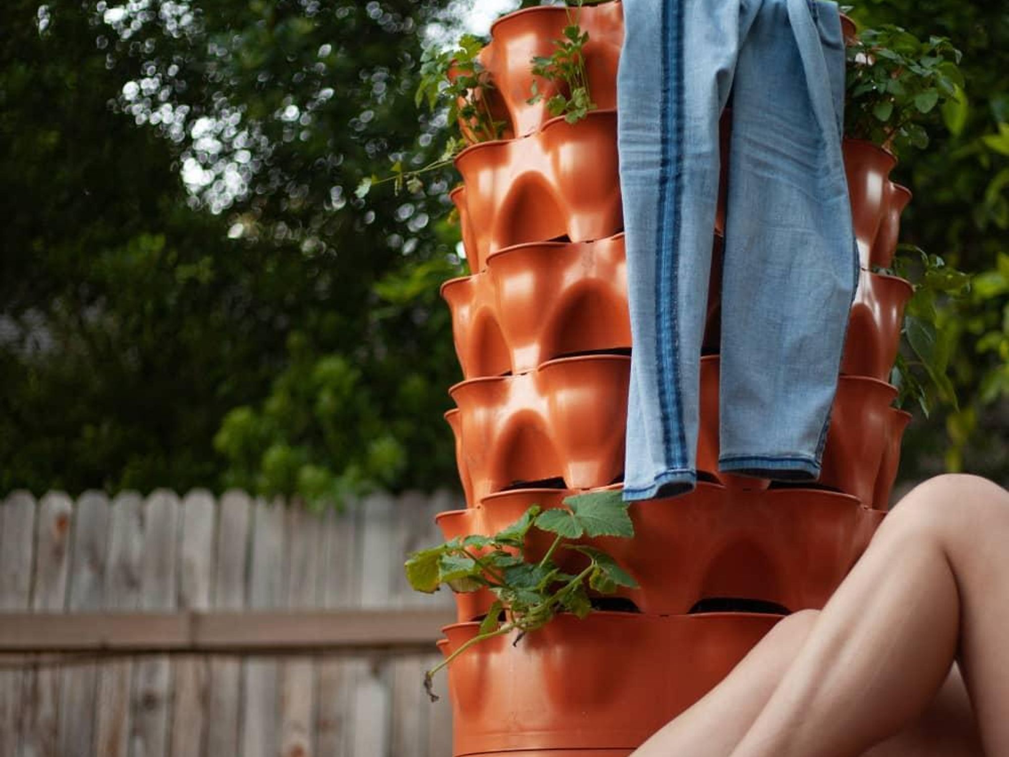 A pair of jeans is hung on a Garden Tower planter, with bare legs in the corner.