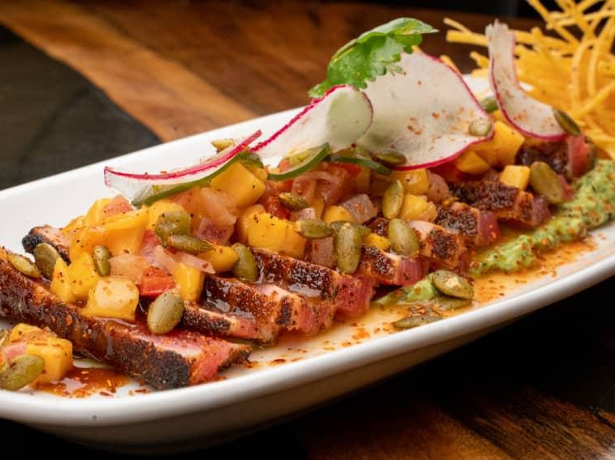 A plate of sliced steak with garnishes including radish and pepitas.