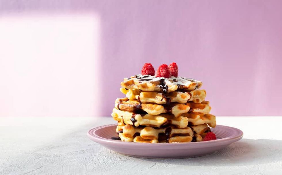 A stack of waffles with chocolate syrup, raspberries and powdered sugar.