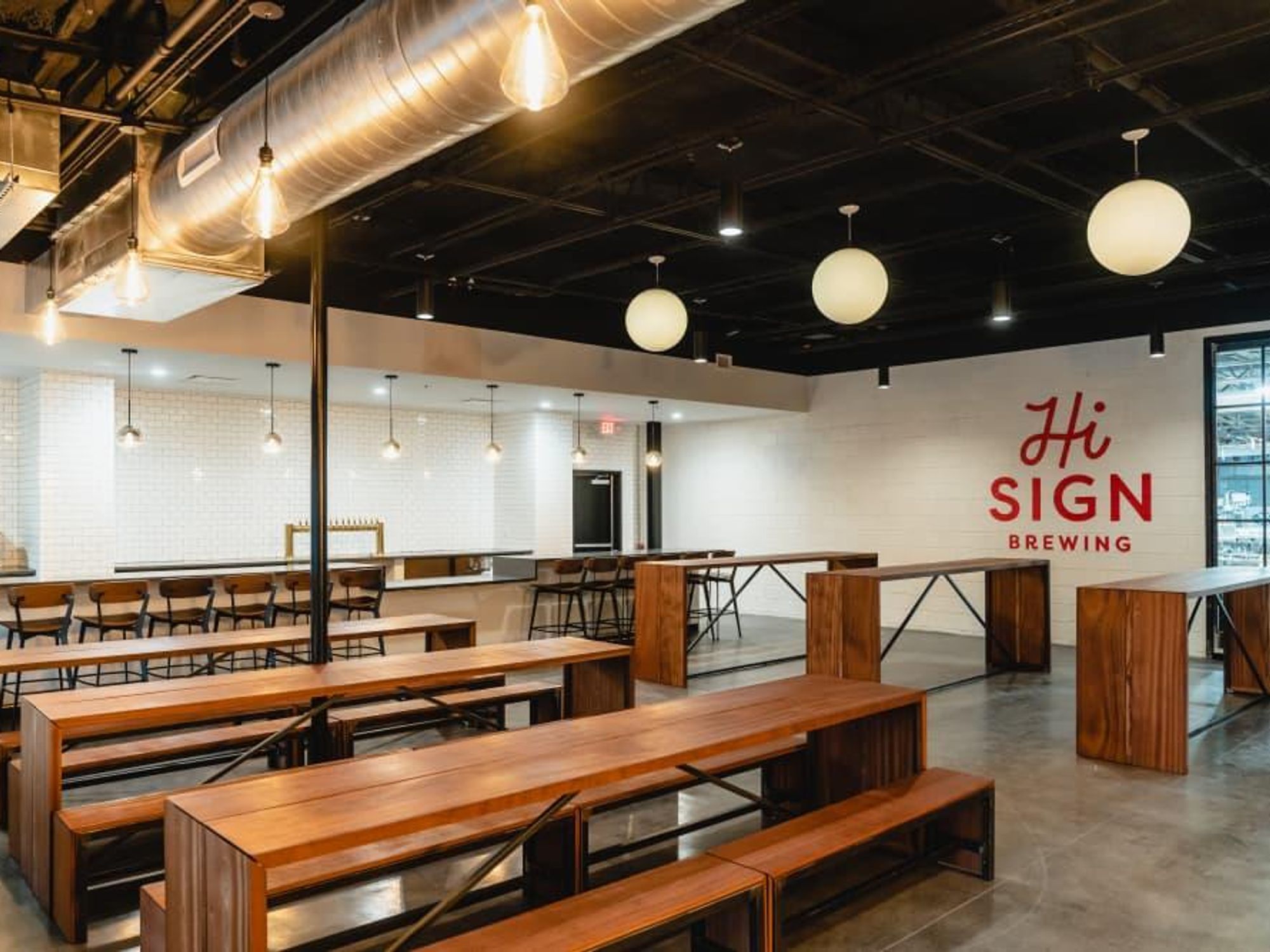 A taproom in natural wood and white, with the new Hi Sign branding on the wall in red.