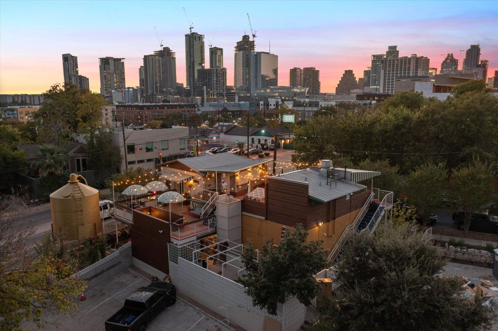 A view of the exterior or Flower Shop Austin, including the rooftop deck, umbrella seating, the water tower, and a view of downtown.