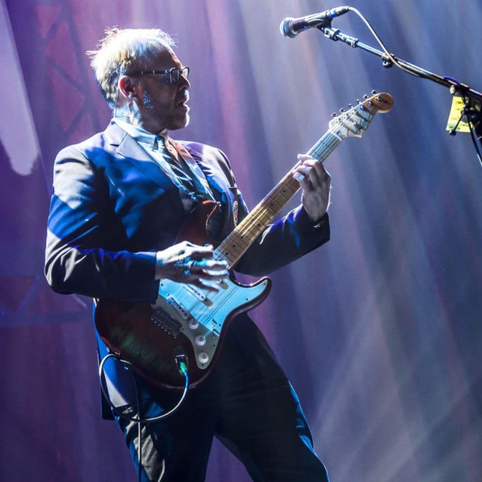 Alton Brown plays an electric guitar onstage.