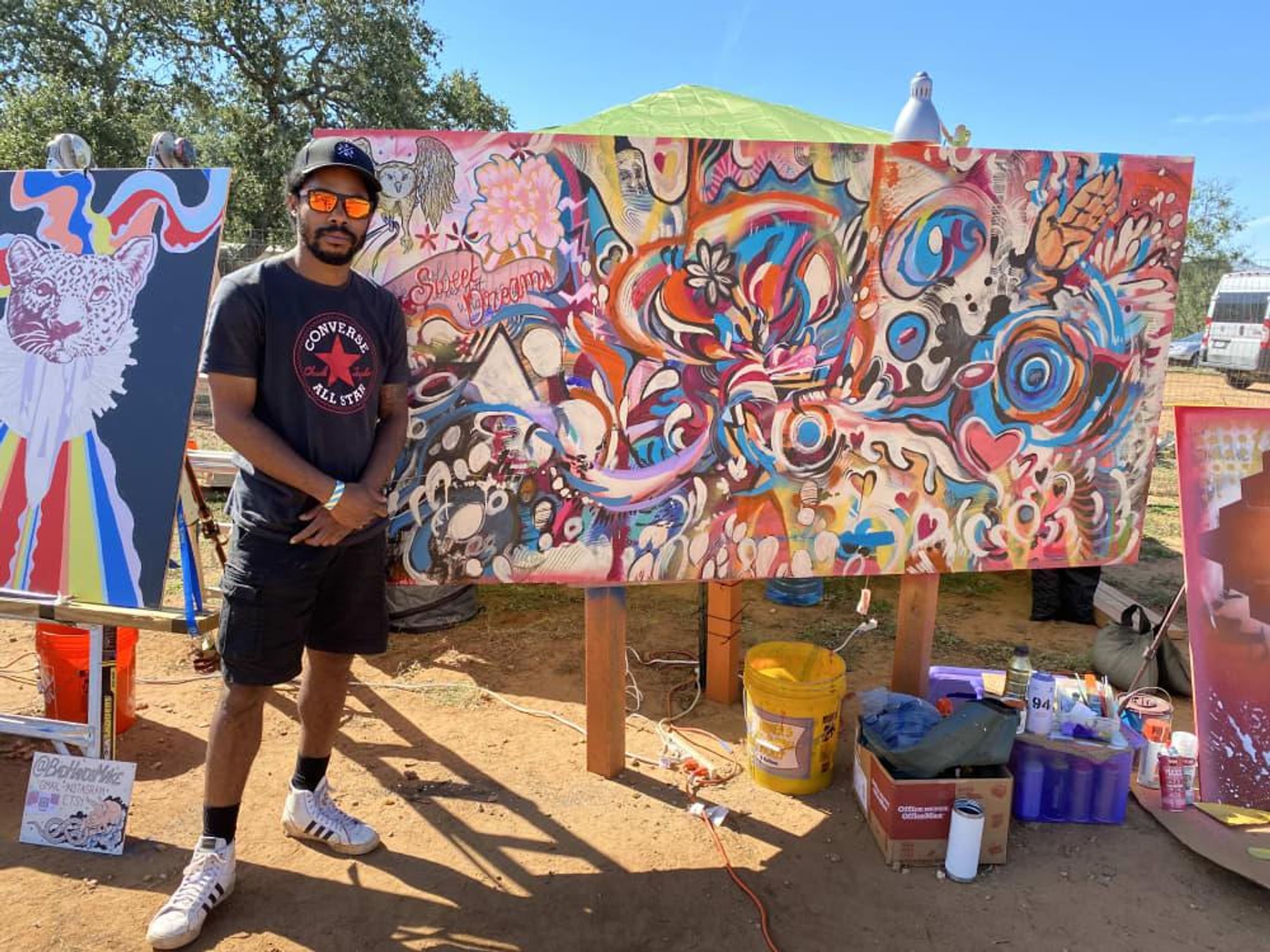 Artist Kel Brown stands next to a large abstract painting featuring bright colors and organic forms.