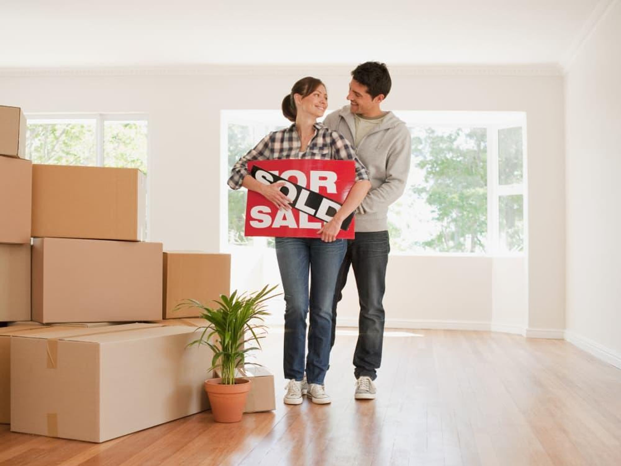Couple with moving boxes and sold sign