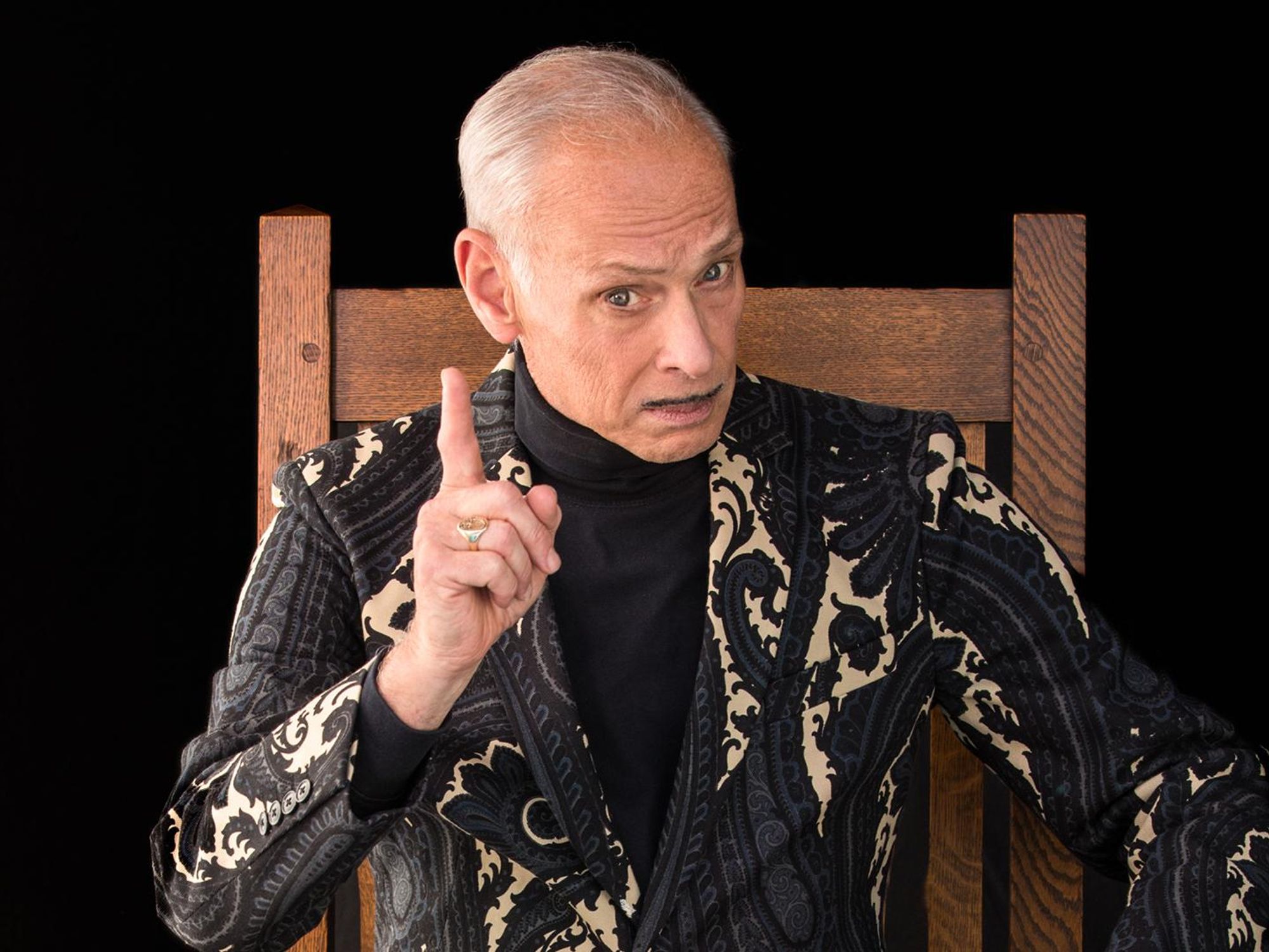 John Waters sitting in a chair.