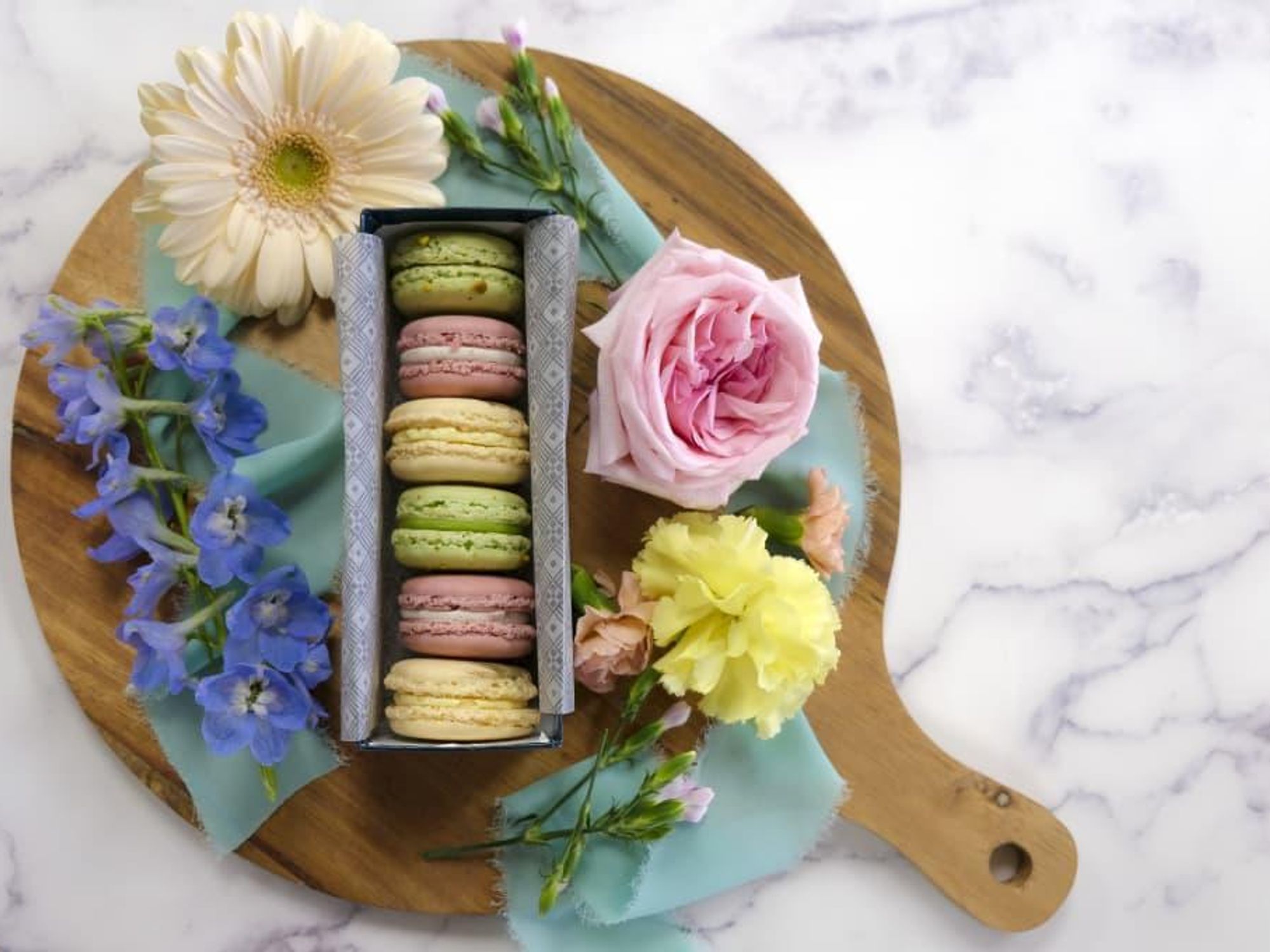 Macarons in pastel colors sit among flowers.
