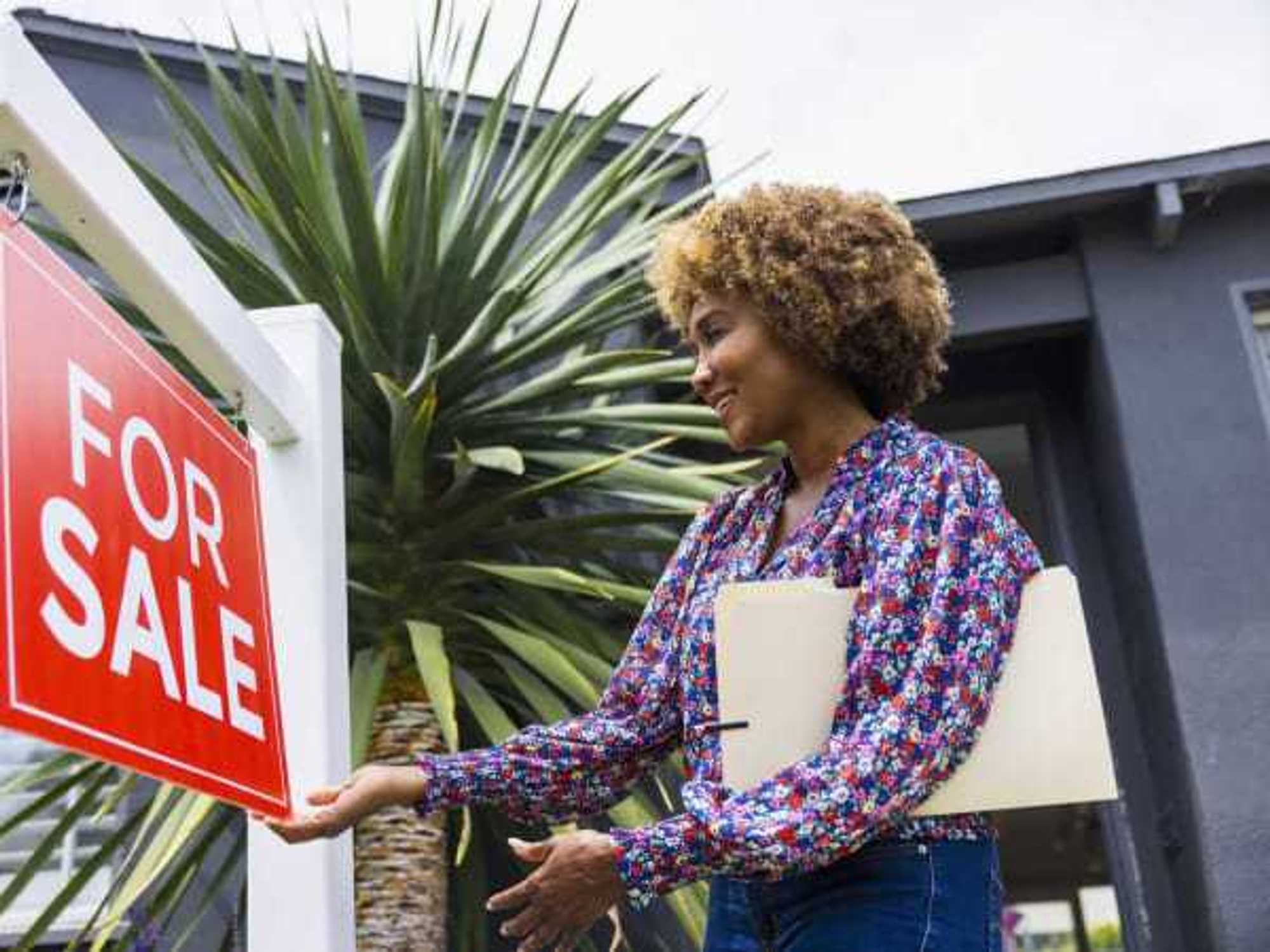 Mature real estate agent adjusting for sale sign in front of home