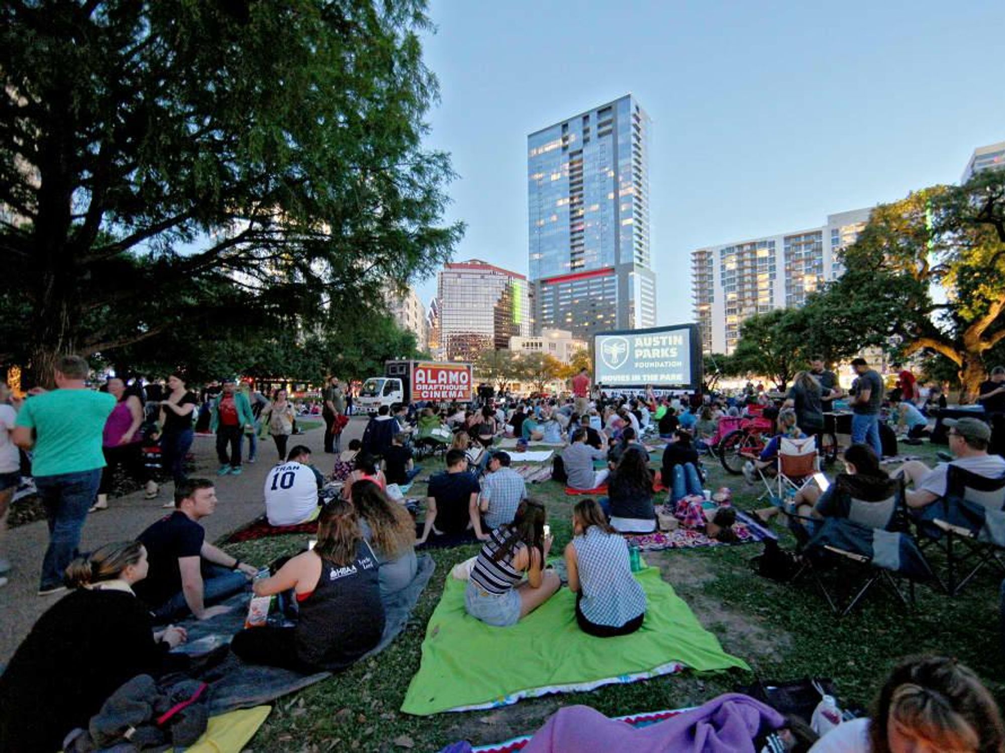 Movie-goers lay out blankets at the park to watch a film in front of the Austin skyline.