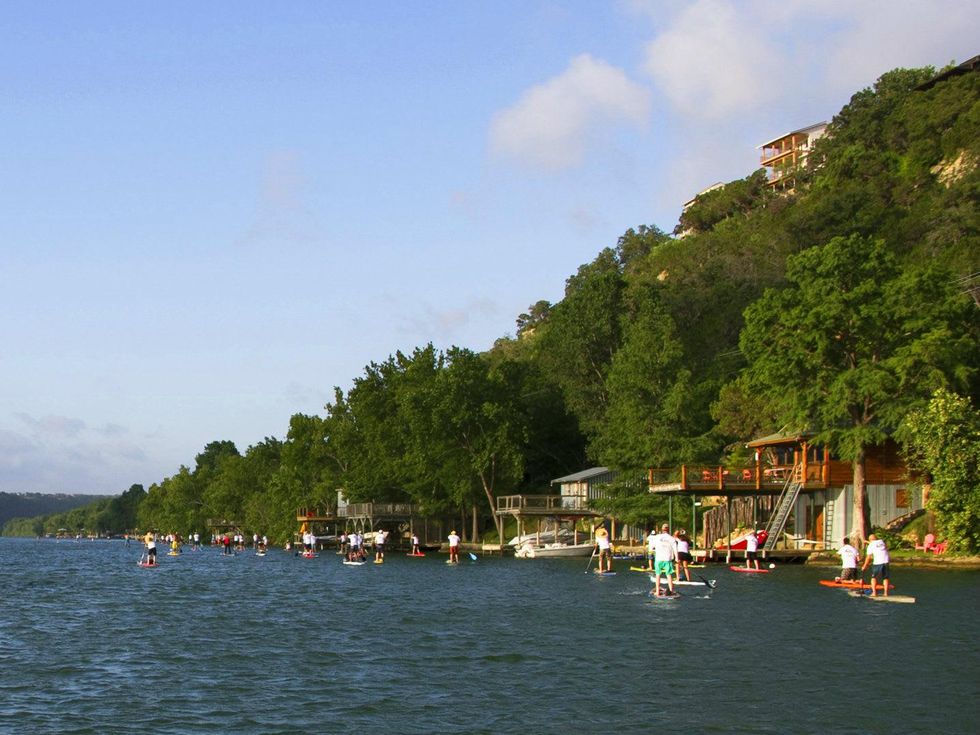 paddleboarders on lake austin in front of hill