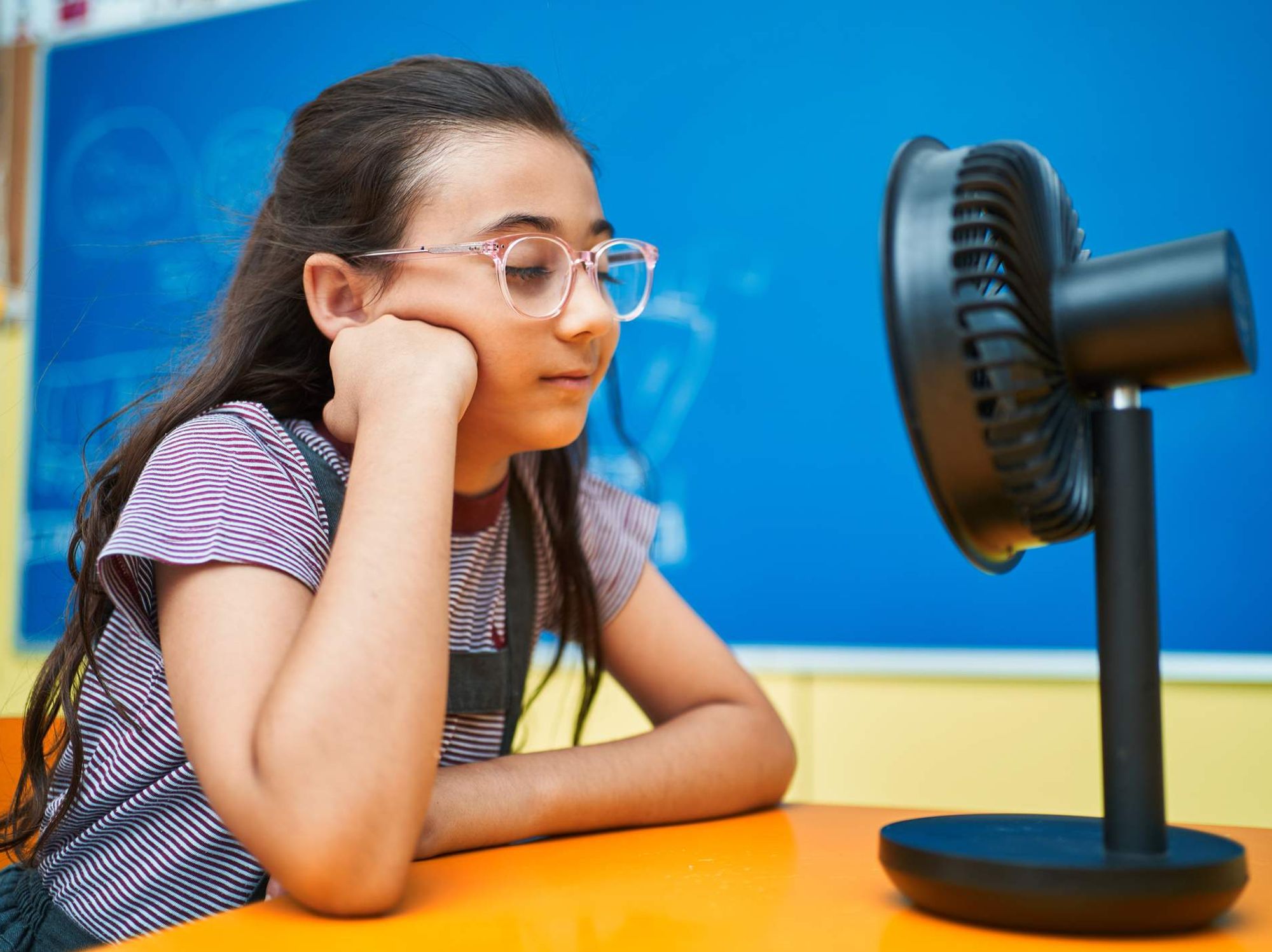 School girl interacting with electric fan at classroom