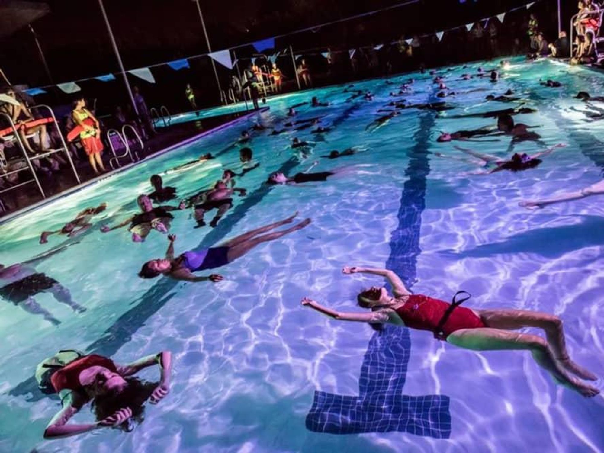 Synchronized swimmers float in a pool lit from below for a Forklift Danceworks project in Austin.