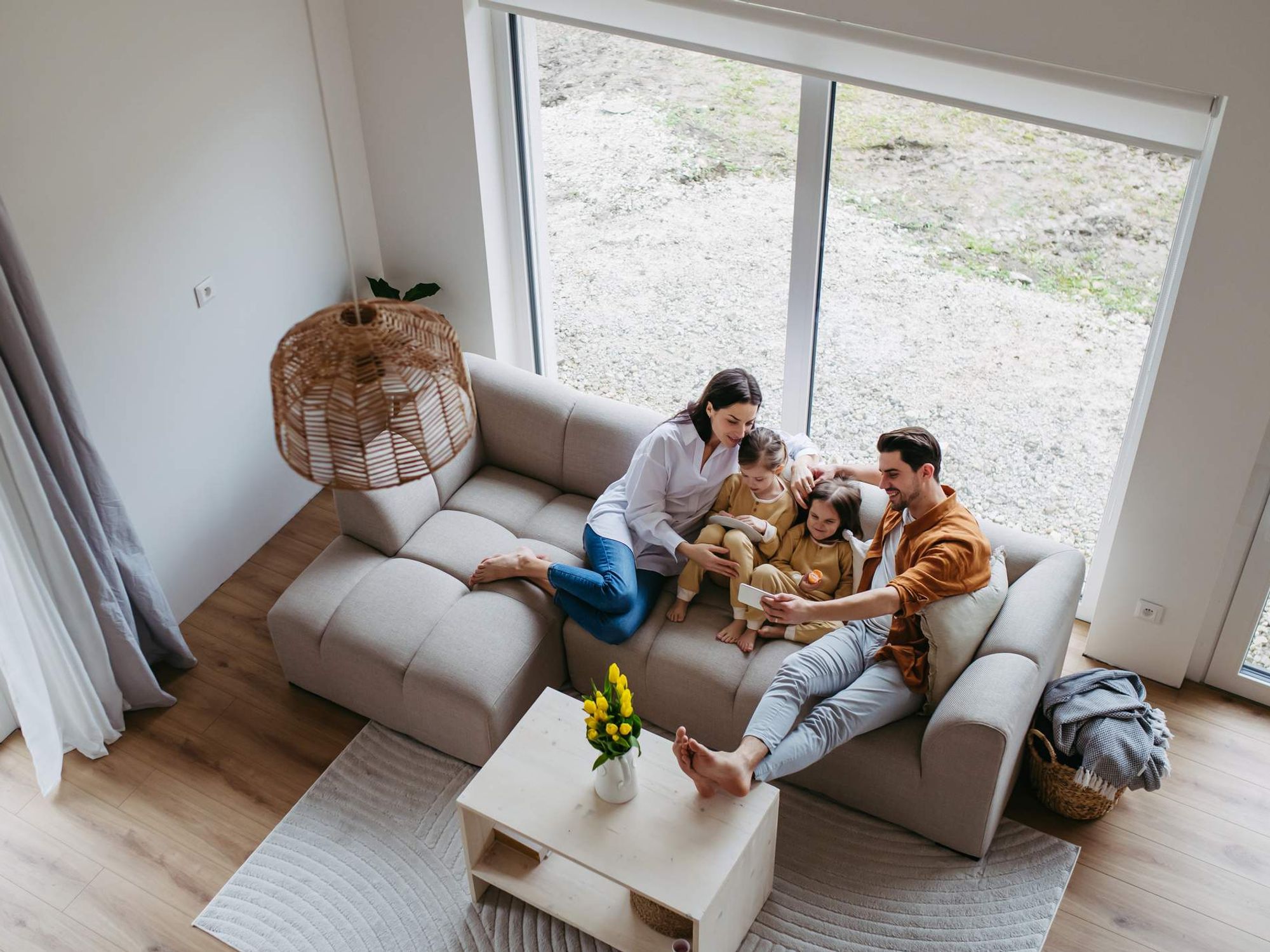 Top view of nuclear family with small daughters sitting on sofa in their new home. Young family buying a first house, big milestone and home ownership concept.