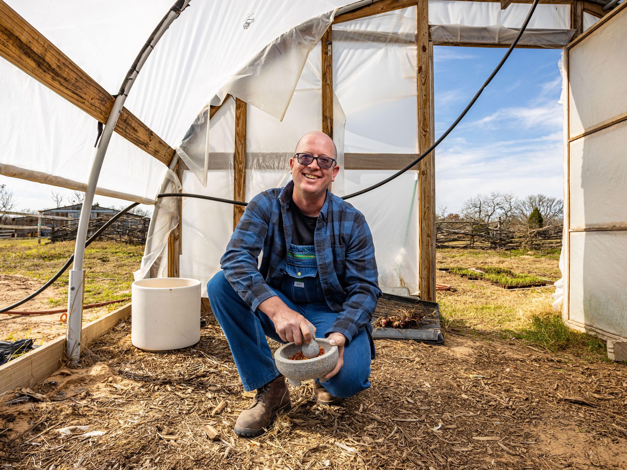 Trosi Farms' Will Nikkel holds a molcajete while kneeling inside an open greenhouse.