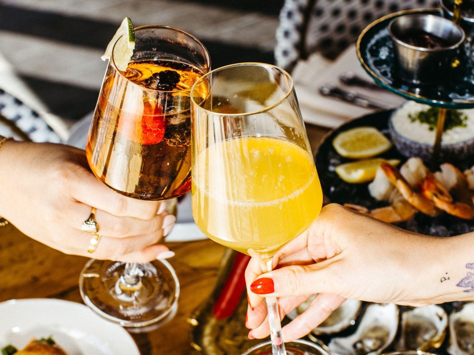 Two glasses clinked in a toast over a table of food at Honey Moon Spirit Lounge.