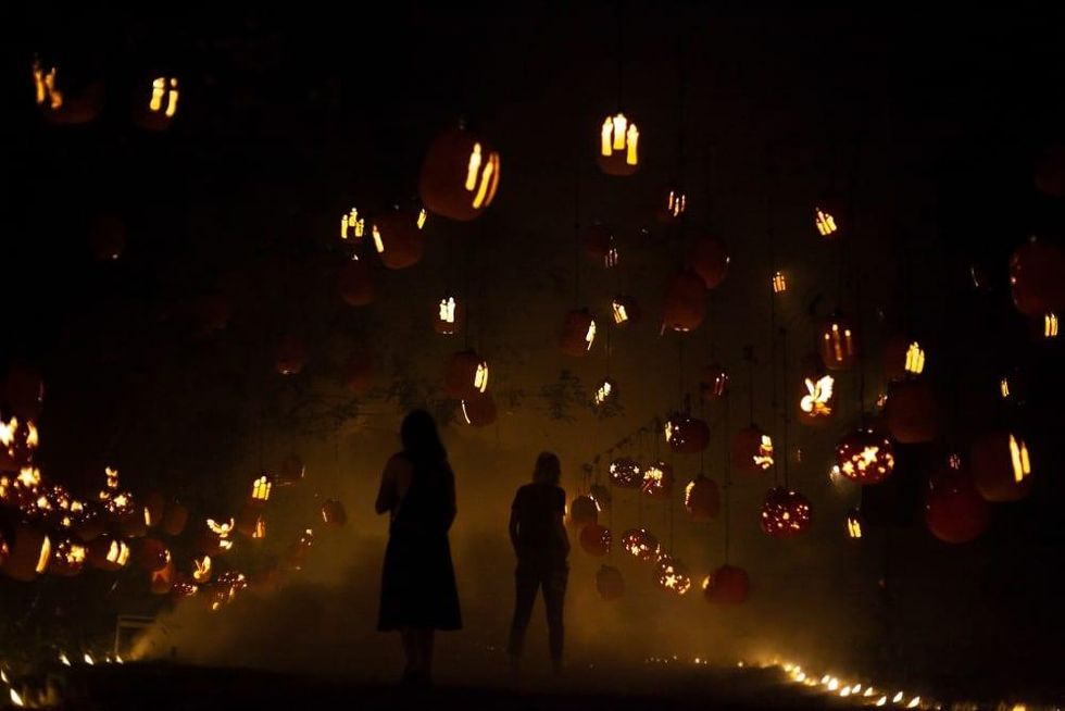 Two shadowed figures wander through a hall of floating jack-o-lanterns in mist.