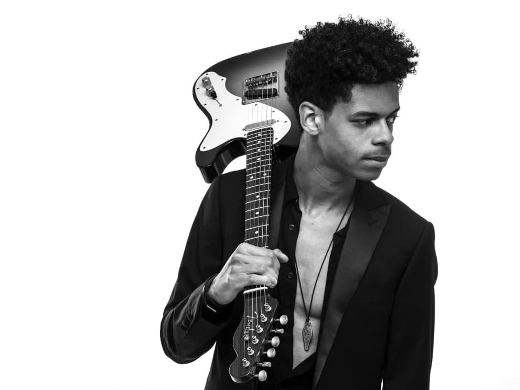 Zach Person poses with an electric guitar over his shoulder, in a tuxedo jacket with an unbuttoned shirt.